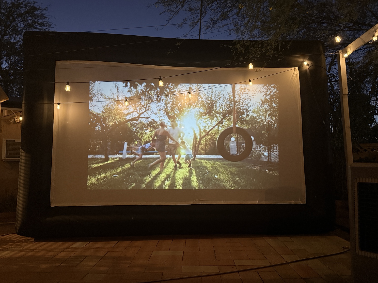 A warm backyard cinema glowing under string lights at sunset